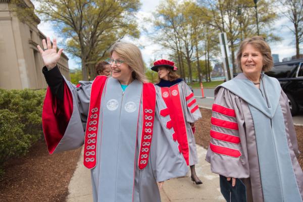 President Kornbluth walks to her Inaugural Ceremony as she smiles and waves to someone off camera.
