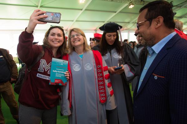 President Kornbluth stands in the middle of students and smiles for a selfie under the inauguration tent.