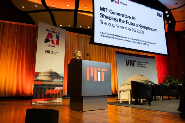 President Kornbluth stands behind a podium on stage beneath a screen that reads MIT Generative AI: Shaping the Future Symposium.